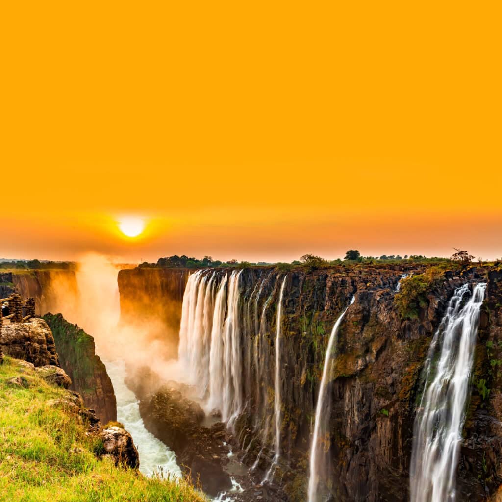 Golden hues of the sunset over Victoria Falls as mist rises from the cascading water during a luxury Zambia safari journey.